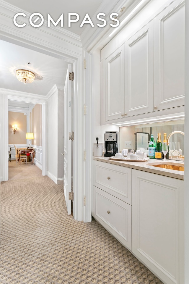 corridor featuring light colored carpet, crown molding, and a sink