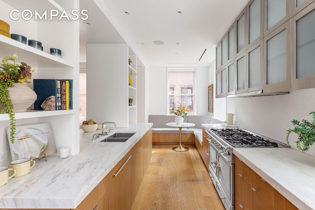 kitchen with range with gas cooktop, glass insert cabinets, light stone counters, open shelves, and a sink