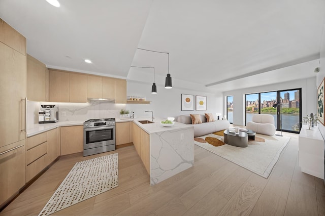 kitchen with light brown cabinets, a sink, open floor plan, stainless steel range with gas cooktop, and a peninsula