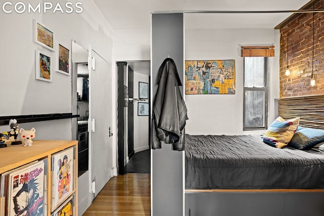 bedroom with dark hardwood / wood-style flooring and brick wall