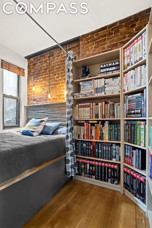 bedroom with brick wall and hardwood / wood-style flooring