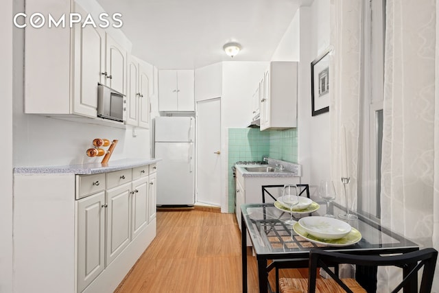kitchen featuring decorative backsplash, light wood-type flooring, light countertops, white cabinets, and freestanding refrigerator