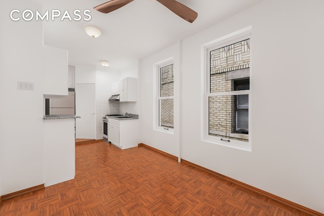kitchen with freestanding refrigerator, a ceiling fan, baseboards, white cabinetry, and gas range