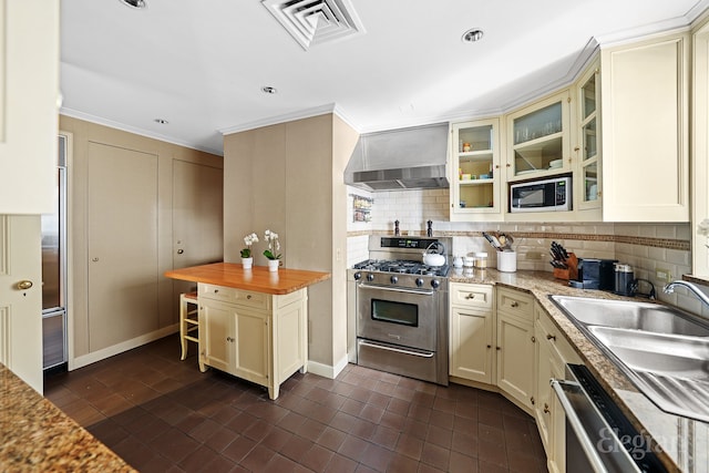 322 E 57th St Unit 12/13B, New York City, NY 10022 - kitchen with stainless steel range with gas stovetop, wall chimney exhaust hood, built in microwave, cream cabinetry, and backsplash