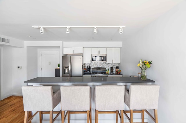 30-25 21st St Unit 2-A, New York City, NY 11102 - kitchen with stainless steel appliances, rail lighting, white cabinetry, a kitchen bar, and wood finished floors