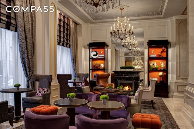 sitting room featuring a high end fireplace, crown molding, a decorative wall, a raised ceiling, and a chandelier