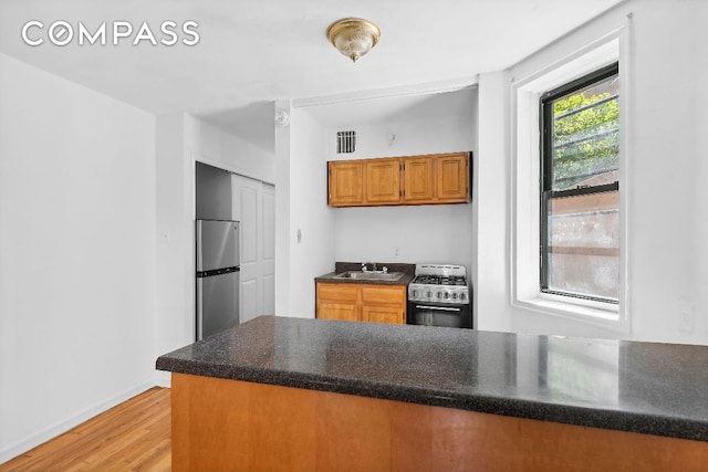 kitchen featuring sink, light wood-type flooring, kitchen peninsula, and appliances with stainless steel finishes