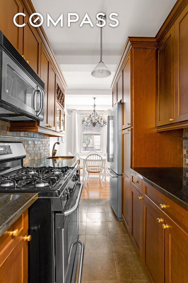 kitchen featuring dark stone countertops, a sink, appliances with stainless steel finishes, a notable chandelier, and tasteful backsplash