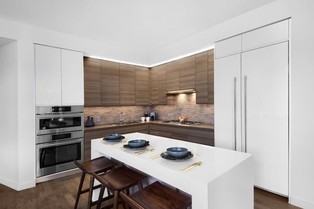 kitchen with appliances with stainless steel finishes, backsplash, sink, white cabinets, and a center island