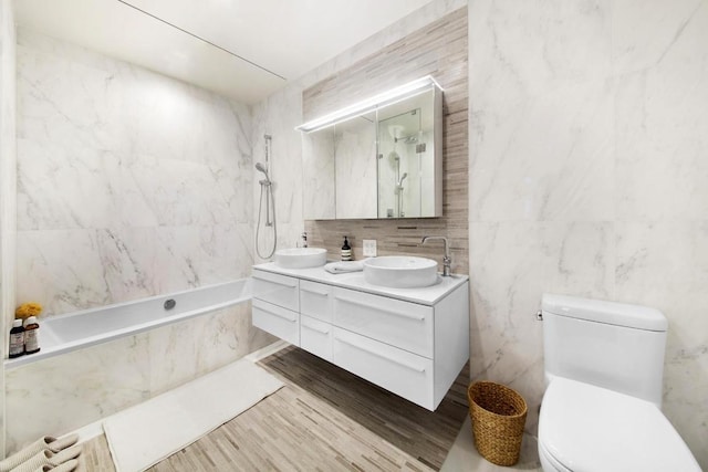 full bathroom with toilet, tiled shower / bath combo, tile walls, wood-type flooring, and vanity