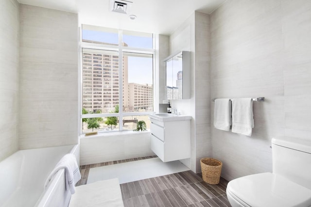 bathroom with toilet, a healthy amount of sunlight, vanity, and tile walls