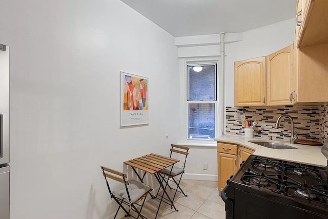 kitchen with tasteful backsplash, black gas stove, light brown cabinets, light tile patterned floors, and a sink