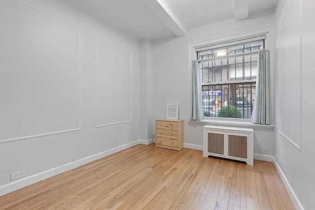 unfurnished room with radiator, light hardwood / wood-style flooring, and beamed ceiling