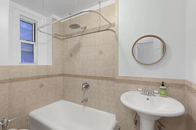 bathroom with tiled shower / bath combo, sink, and tile walls