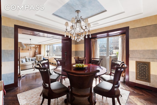 dining space with a wealth of natural light, a raised ceiling, and a notable chandelier