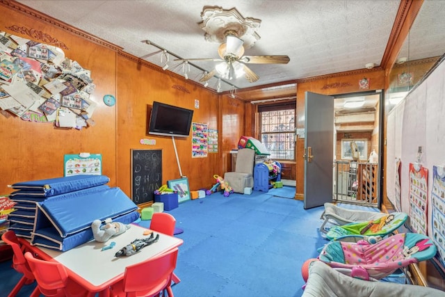 rec room with a textured ceiling, ceiling fan, and wood walls