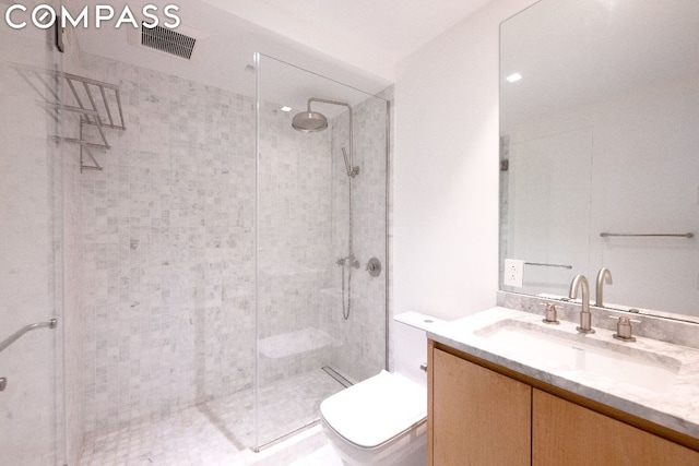 bathroom with toilet, tiled shower, and vanity