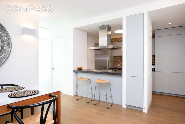 kitchen with gas stovetop, light wood finished floors, dark countertops, island range hood, and modern cabinets