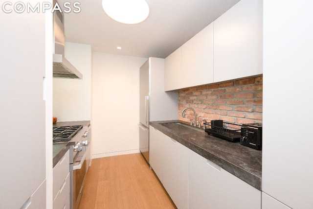 kitchen with white cabinetry, wall chimney range hood, sink, wall oven, and light wood-type flooring