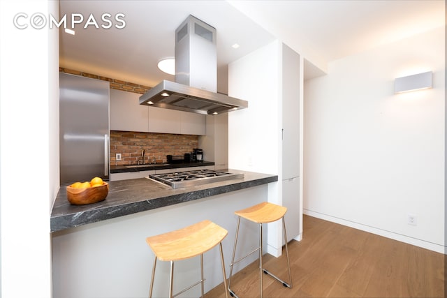 kitchen with decorative backsplash, dark countertops, appliances with stainless steel finishes, island exhaust hood, and a sink