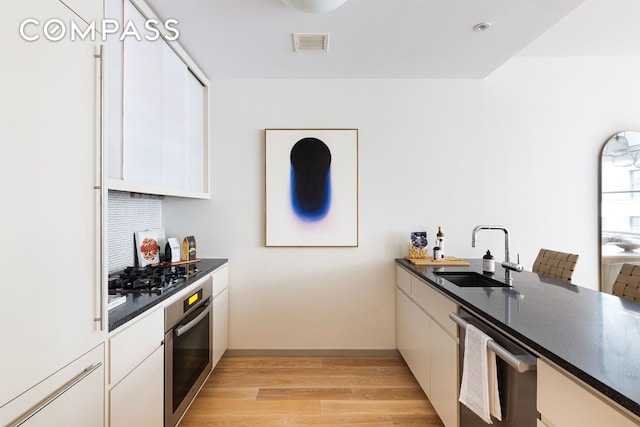 kitchen featuring stainless steel appliances, dark countertops, a sink, and white cabinetry