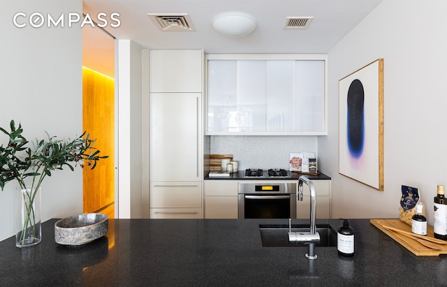 kitchen featuring paneled built in refrigerator, visible vents, stainless steel oven, white cabinets, and dark countertops