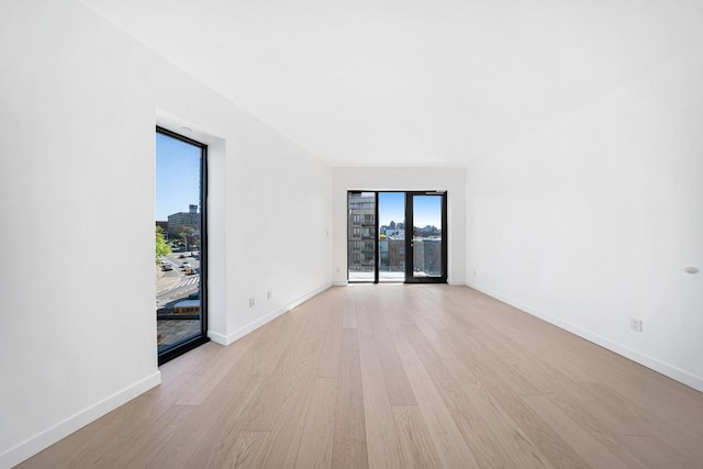 empty room featuring baseboards, french doors, light wood-type flooring, and a healthy amount of sunlight