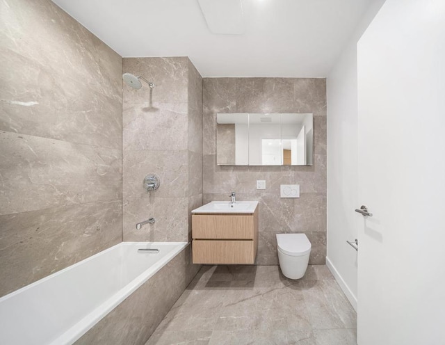 bathroom featuring tiled shower / bath, vanity, toilet, and tile walls