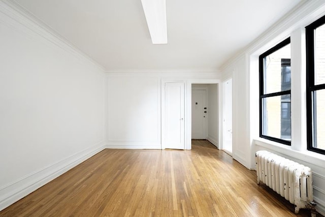 spare room featuring light hardwood / wood-style flooring, radiator heating unit, ornamental molding, and a healthy amount of sunlight