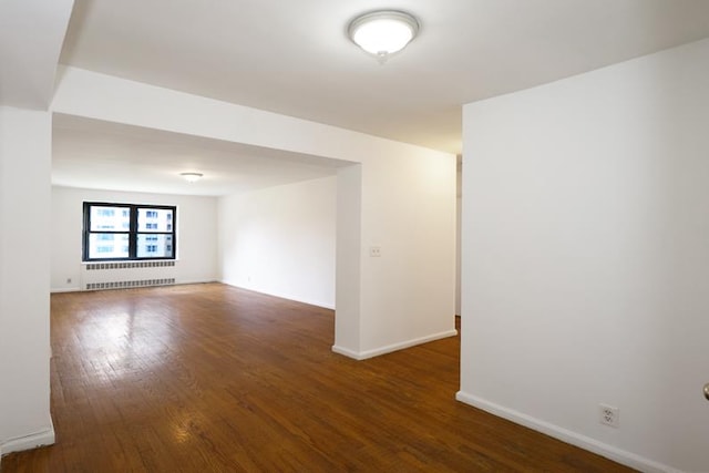 unfurnished room featuring baseboards, wood finished floors, and radiator heating unit