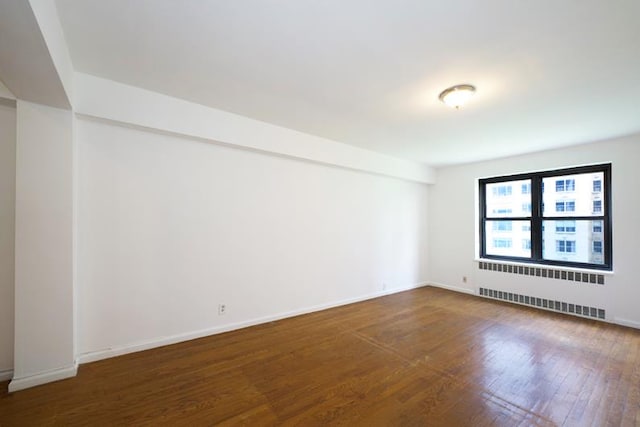 spare room featuring radiator, wood finished floors, and baseboards