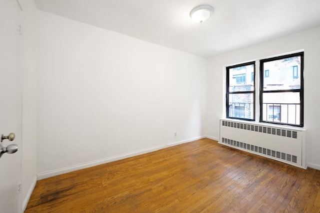 empty room with baseboards, radiator, and wood finished floors