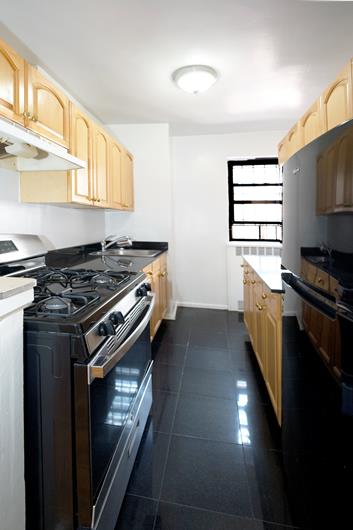 kitchen featuring stainless steel gas range oven, dark tile patterned floors, under cabinet range hood, light brown cabinetry, and a sink