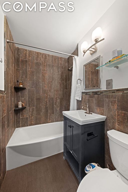 full bathroom featuring tile walls, toilet, vanity, and shower / bath combo