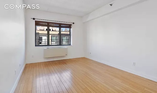 empty room featuring radiator heating unit and light wood-type flooring