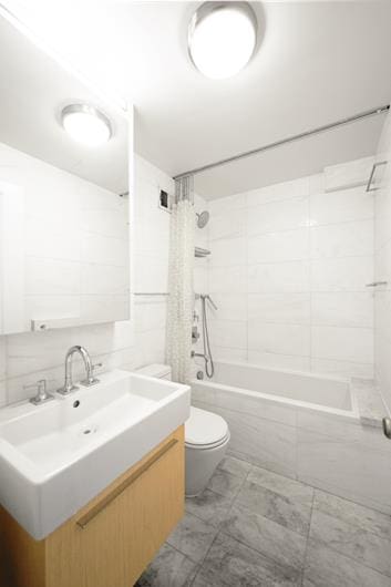 full bathroom with marble finish floor, tile walls, toilet, tiled shower / bath combo, and vanity