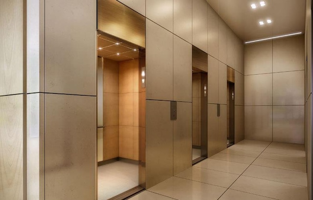 corridor featuring elevator, light tile patterned floors, and tile walls