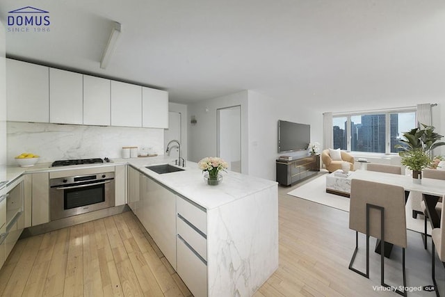 kitchen with sink, gas stovetop, white cabinetry, stainless steel oven, and decorative backsplash