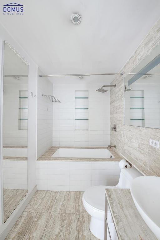 bathroom with toilet, a tile shower, vanity, and tile walls