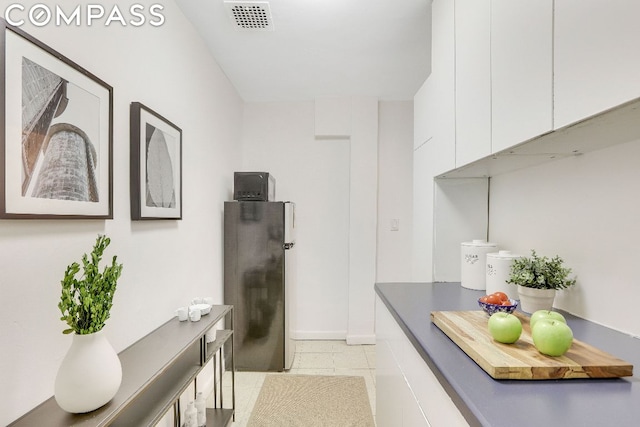 interior space featuring white cabinetry, light tile patterned floors, and stainless steel refrigerator