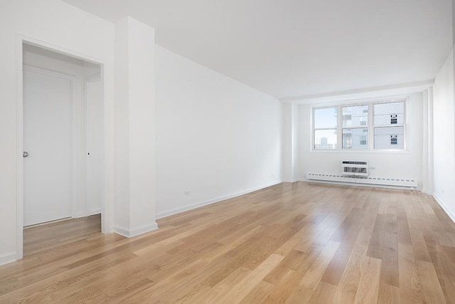 spare room with a baseboard heating unit, light wood-type flooring, baseboards, and a wall unit AC