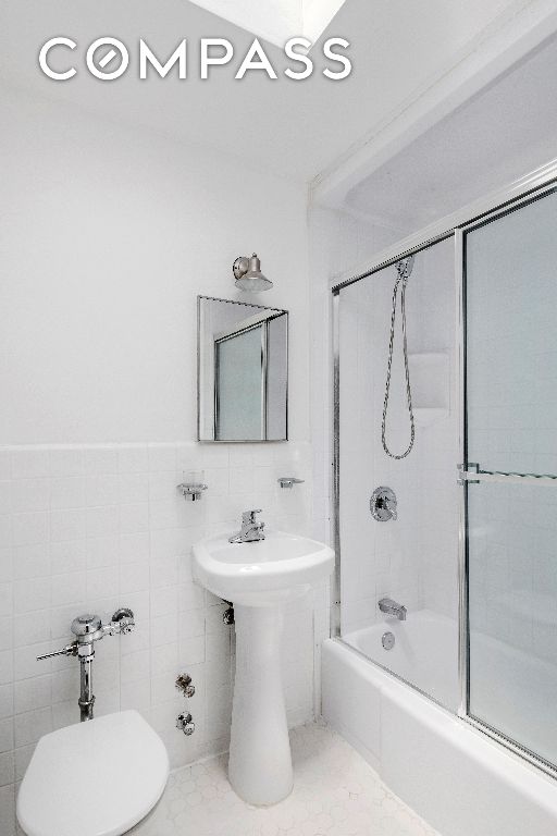 bathroom with toilet, bath / shower combo with glass door, and tile walls