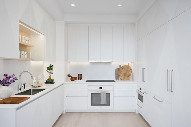 kitchen with modern cabinets, a sink, white cabinetry, light countertops, and white oven