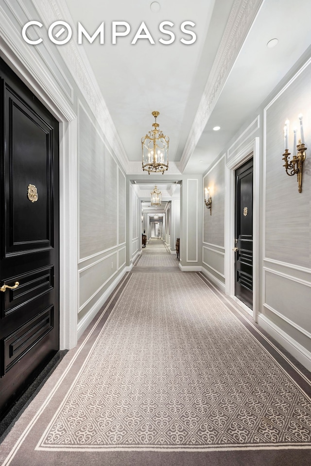 corridor featuring carpet floors, a chandelier, crown molding, and a decorative wall