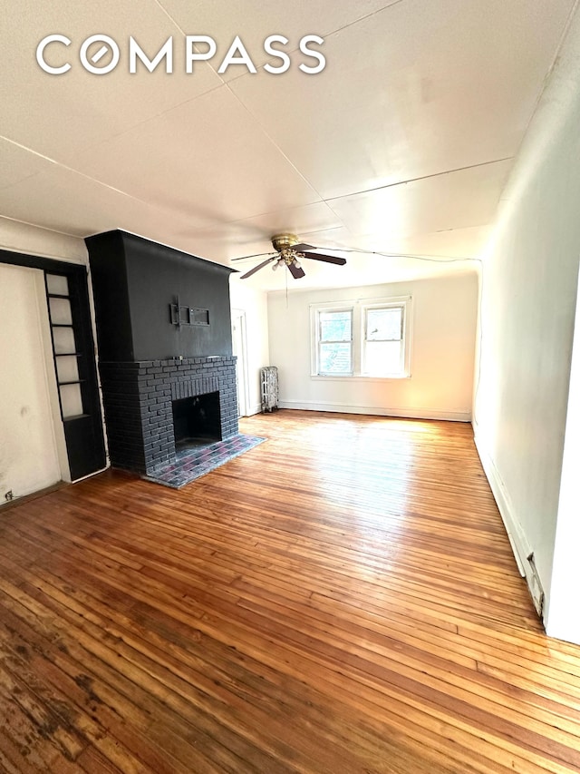 unfurnished living room with hardwood / wood-style flooring, a fireplace, baseboards, and a ceiling fan