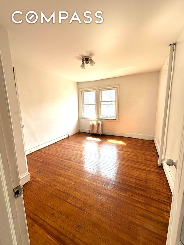 unfurnished room with a baseboard heating unit, radiator heating unit, baseboards, and wood-type flooring