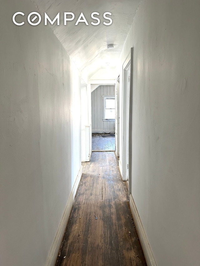 hallway with vaulted ceiling, hardwood / wood-style flooring, and baseboards