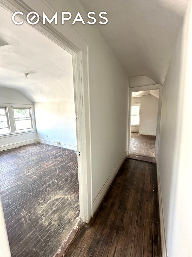 hallway with dark wood-style floors, lofted ceiling, and baseboards