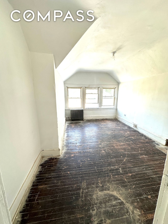 additional living space with lofted ceiling, baseboards, wood finished floors, and radiator