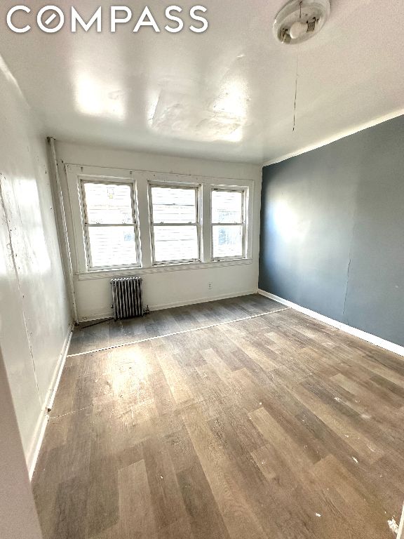 empty room with wood-type flooring and radiator heating unit